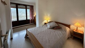Ein Schlafzimmer mit einem Bett, zwei Nachttischlampen, einem Fenster mit Vorhängen und einer Heizung.