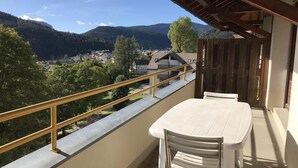 Ein Balkon mit Tisch und Stühlen, der auf eine gebirgige Landschaft mit Häusern und Bäumen blickt.