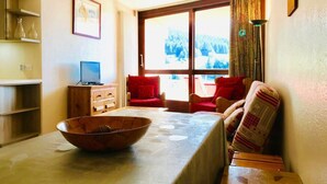 A living room with a wooden table, a large bowl, a television, and two red chairs.