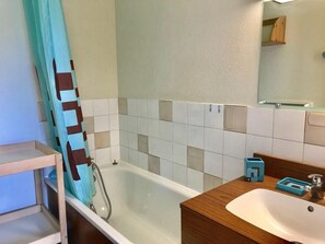 Un baño con una bañera, un lavabo y un espejo. Hay un perchero y una estantería con artículos de aseo.