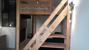Una cama nido con escalera de madera, una mesa de comedor con dos cuencos, y una silla.