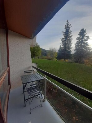 A balcony with a table and chairs, overlooking a grassy area with trees and a hill in the background. - 2nd floor, balcony, parking, tv, 20m², Villard de Lans (Villard-de-Lans)
