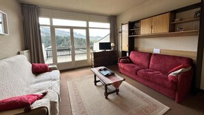 Habitación de hotel con una cama, un sofá rojo, una mesa de centro y vistas a las montañas a través de la ventana.