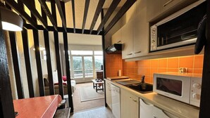 Cocina compacta con microondas, horno y pileta. Se ve un comedor con banco a través de una puerta abierta.