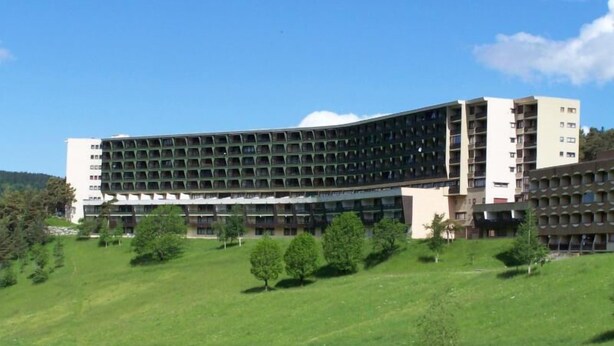 Un hotel grande de varios pisos con fachada curva, rodeado por un área verde con árboles.
