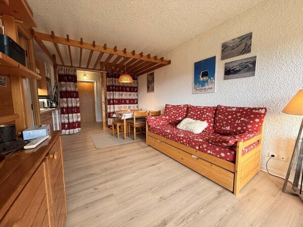 A cozy room with a wooden sofa, a dining table, and a kitchen area.
