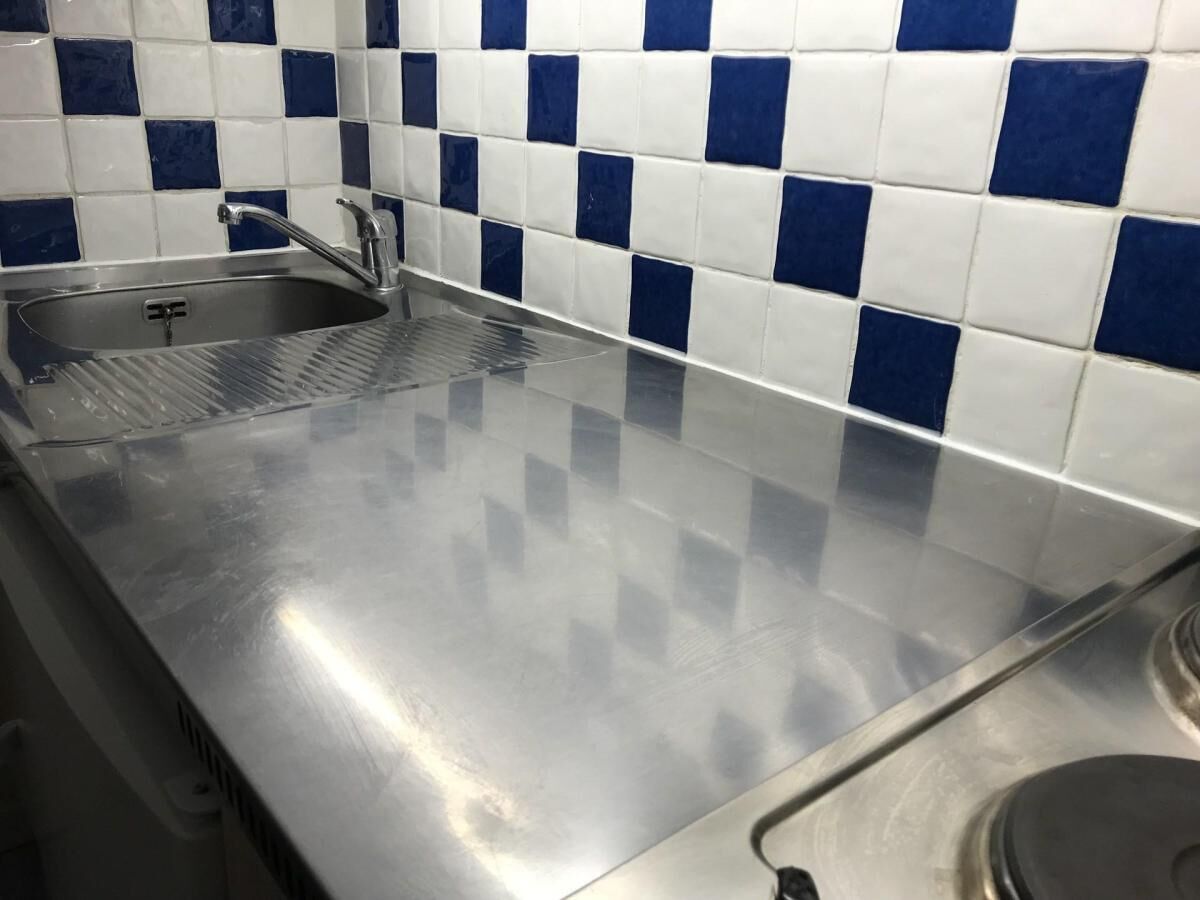 Een aanrecht van roestvrij staal met een spoelbak en een achterwand van blauwe en witte tegels.