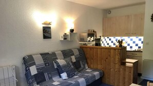 Ett kompakt bostadsutrymme med en soffa klädd i olika tygbitar, ett litet köksområde och ett matbord.