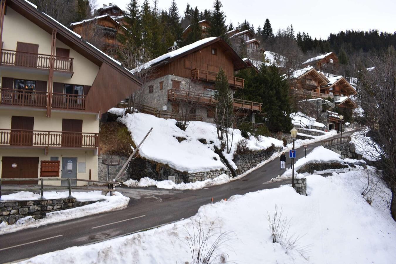 A snow-covered mountain village with wooden buildings, a road, and a person walking.