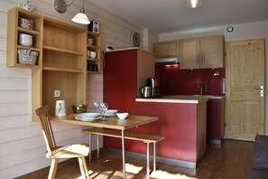 A compact kitchen with wooden cabinets, a red accent wall, and a dining area with a wooden table and chair.