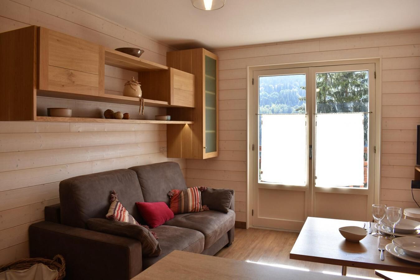 A cozy living room with a sofa, wooden shelves, and a dining table with plates and glasses.