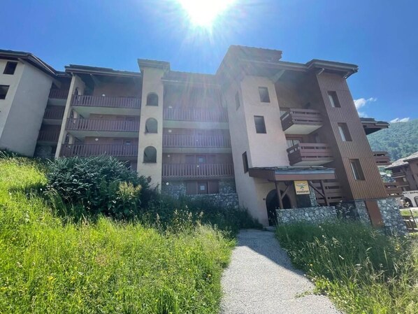A multi-story building with balconies, a gravel path, and surrounding greenery.