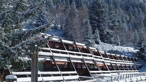 Un edificio cubierto de nieve con techo inclinado, rodeado de árboles cargados de nieve.