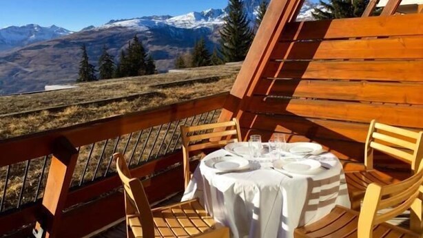 Comedor con una mesa dispuesta para dos personas, con vistas a un paisaje montañoso.