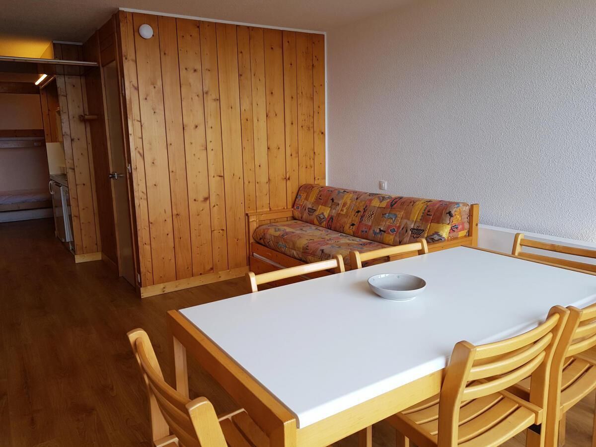 Un comedor con una mesa blanca y sillas de madera, un armario de madera y un sofá colorido.