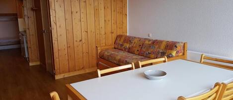 Un comedor con una mesa blanca y sillas de madera, un armario de madera y un sofá colorido.