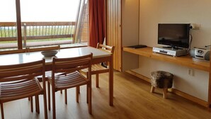 Una habitación con una mesa de comedor, sillas, un televisor y un taburete pequeño.