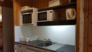 Una cocina compacta con lavamanos, microondas, hervidor y escurreplatos.