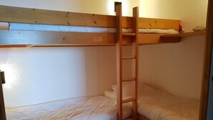 Una cama litera con escalera, cabecero de madera y repisa sobre la cama superior.