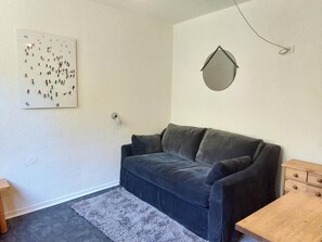 A room with a dark blue sofa, a small wooden table, a white wall with a framed picture, and a round mirror. - 7th floor, tv, 13m², Les Arcs (Les Arcs)