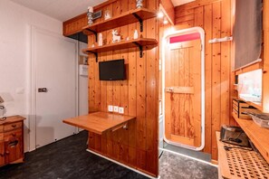 A compact room with wooden walls, a mounted TV, a small table, and a door with a mirror. - 7th floor, tv, 13m², Les Arcs (Les Arcs)