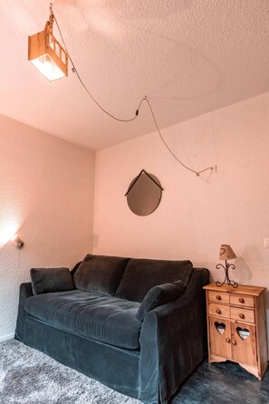 A small, cozy room with a dark-colored sofa, a wooden cabinet with heart-shaped cutouts, and a wall-mounted light fixture. - 7th floor, tv, 13m², Les Arcs (Les Arcs)