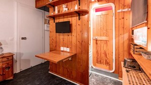 Ett litet rum med träväggar, en väggmonterad TV, ett litet bord och en dörr med en spegel.