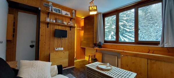 A cozy cabin interior with wooden walls, a television mounted on the wall, a window with a snowy view, and a small table with a tray. - 7th floor, tv, 13m², Les Arcs (Les Arcs)