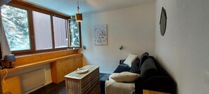 A cozy room with a wooden bench, a small table with a tray, a sofa with cushions, and a large window with a view of trees. - 7th floor, tv, 13m², Les Arcs (Les Arcs)