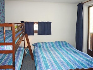 A room with bunk beds, a window with curtains, and a patterned bedspread.