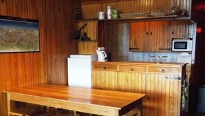 A wooden interior with a dining table and chairs, a kitchen area with a microwave, and a painting on the wall.