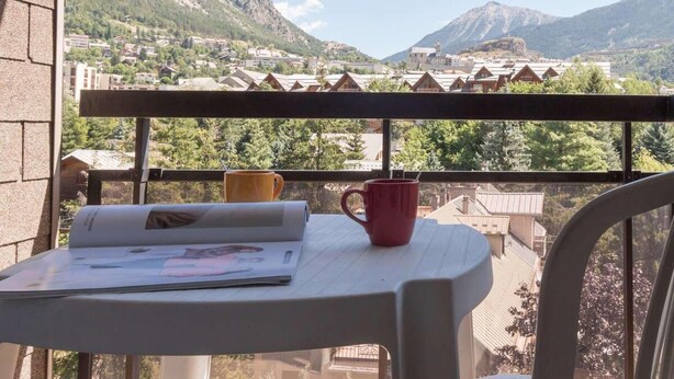 A balcony with a table, two chairs, and a red mug.