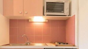 A compact kitchen with pink cabinets, a microwave, a sink, and a dishwasher.