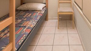 A small, compact room with a bunk bed, a single chair, and a wall-mounted light fixture.