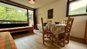 Un comedor con una mesa preparada para dos personas, sillas de madera, un banco y vistas a zonas verdes al exterior.