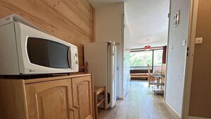Un pasillo estrecho con armarios de madera, un microondas y un refrigerador.