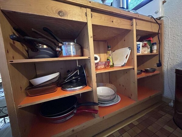 A wooden kitchen shelf with cookware, a kettle, and kitchen essentials.