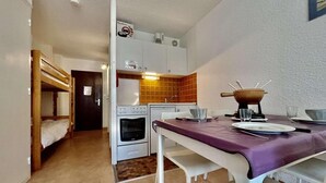 A compact kitchen with white cabinets, a wooden bench, and a dining table with a purple tablecloth. - 150m from ski slopes, 3rd floor, balcony, parking, 28m², Serre Chevalier (SERRE CHEVALIER)