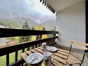 A balcony with a table set for two, overlooking a mountainous landscape.