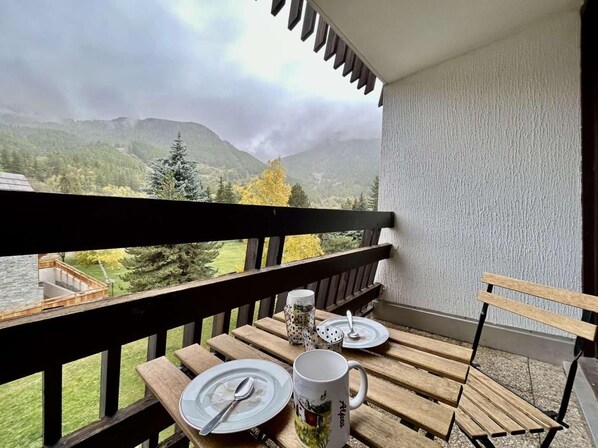 Un balcon avec une table dressée pour deux personnes, offrant une vue sur un paysage montagneux.