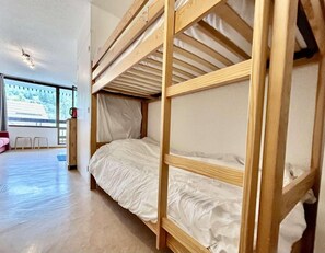Un lit superposé avec une structure en bois et une literie blanche, dans une pièce dotée d’une grande fenêtre donnant sur la forêt.