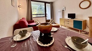 A dining area with a table set for two, a television, and a window with curtains. - 150m from ski slopes, 3rd floor, balcony, parking, 28m², Serre Chevalier (SERRE CHEVALIER)
