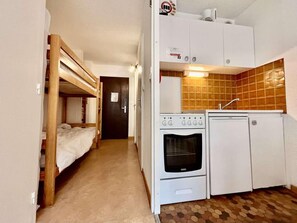 A compact room with a bunk bed, a kitchenette with a stove and refrigerator, and a tiled backsplash.