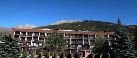 A multi-story building with a flat roof, surrounded by trees and mountains in the background.