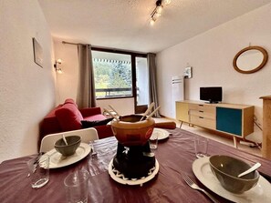 A dining area with a table set for two, a television, and a window with curtains.