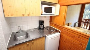 Eine kompakte Küche mit Holzschränken, einer Edelstahl-Spüle, einer Mikrowelle und einem kleinen Kühlschrank.