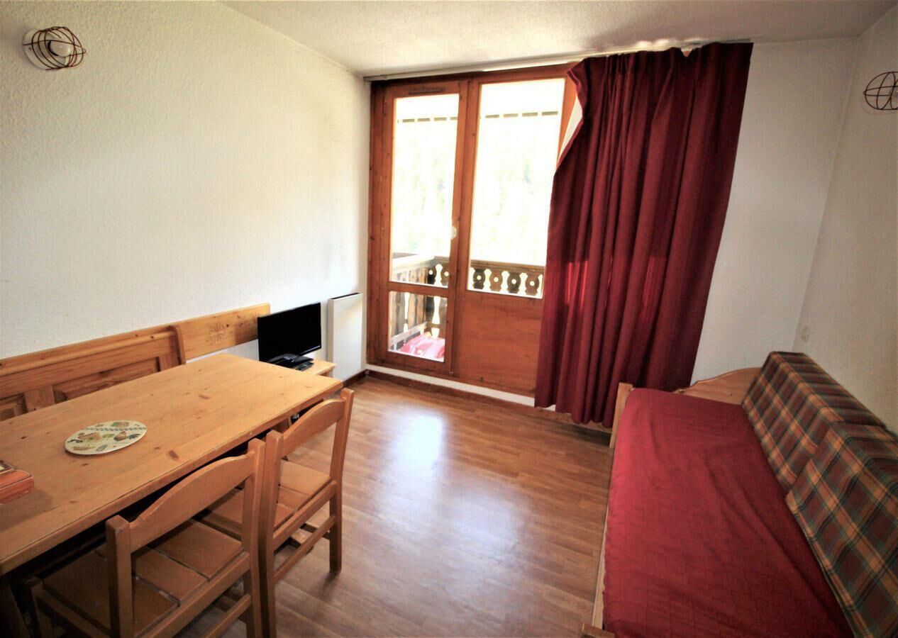 A small room with a wooden table, chairs, a sofa, and a window with curtains.