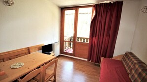 Ein kleiner Raum mit einem Holztisch, Stühlen, einer Couch und einem Fenster mit Vorhängen.