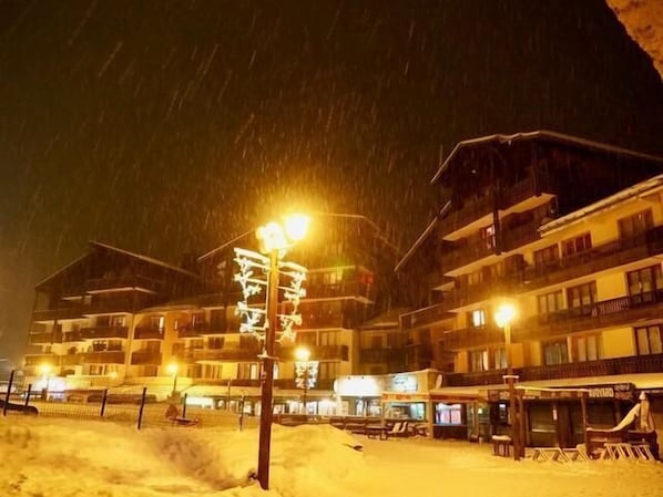 A snow-covered hotel with multiple floors, outdoor seating, and a visible signboard.