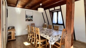 Un comedor con una mesa y sillas de madera, techo con vigas a la vista y una ventana con cortinas.